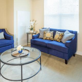 A cozy living room with blue sofas, a glass coffee table, and decorative pillows.