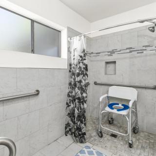 An accessible bathroom with a wheelchair, grab bars, and tiled walls.
