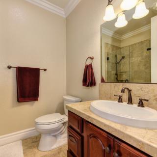 A well-lit bathroom featuring a sink, mirror, and toilet with decorative towels.
