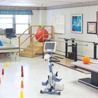 A physical therapy room equipped with various rehabilitation tools including a stationary bike, exercise balls, and parallel bars.