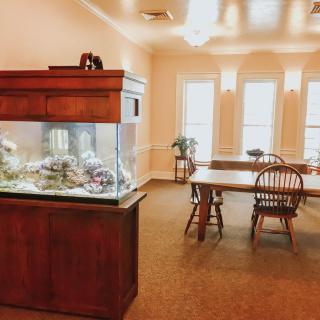 A cozy room with an aquarium, wooden table, and chairs by large windows.