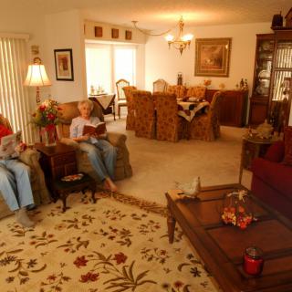 A cozy living room with a dining area in the background, where people are relaxing and reading.