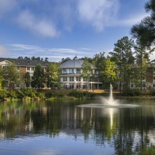 A serene view of a lake with a fountain, surrounded by buildings and trees.