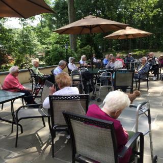 A group of elderly individuals sitting outdoors on a patio, enjoying a sunny day under large umbrellas.