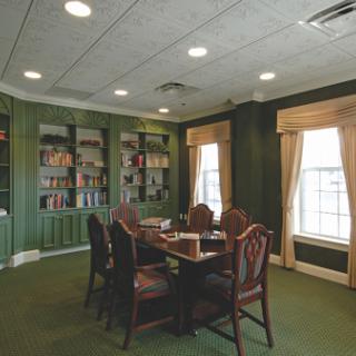 A cozy meeting room with green walls, a wooden table surrounded by chairs, and a bookshelf filled with books.