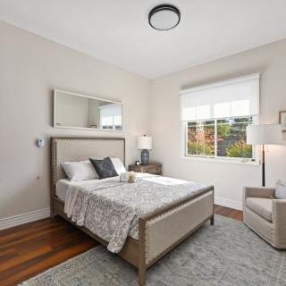 A modern bedroom with neutral tones, featuring a bed with pillows and a bedside table lamp.