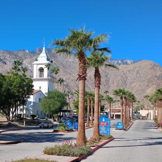 A picturesque scene featuring a church framed by palm trees and mountains under a clear blue sky.