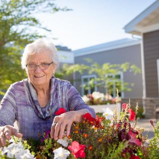 An elderly woman enjoying gardening in the outdoors surrounded by vibrant flowers.