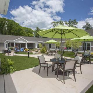 A tranquil patio area with tables, chairs, and green umbrellas in a landscaped residential setting.