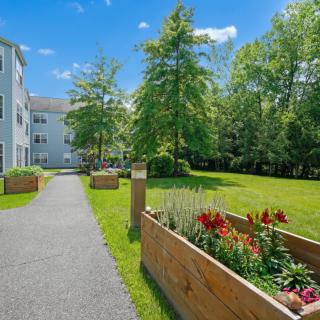 A landscaped garden with a pathway, flower beds, and trees adjacent to a building.