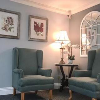 A cozy living room corner featuring two elegant chairs, a lamp on a side table, and decorative wall art.
