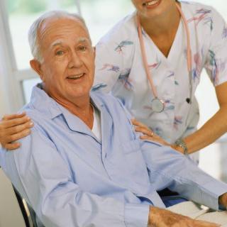A caregiver assisting an elderly man in a wheelchair indoors.