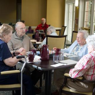 A group of elderly people sitting around a table, engaged in conversation at a dining area.