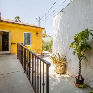 A sunny patio with a yellow exterior wall, potted plants, and a ramp with railings.