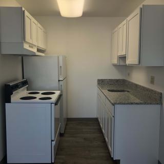 A compact apartment kitchen with white cabinets and modern appliances.