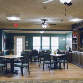 A cozy dining area with several tables and chairs, wooden flooring, and a ceiling fan.