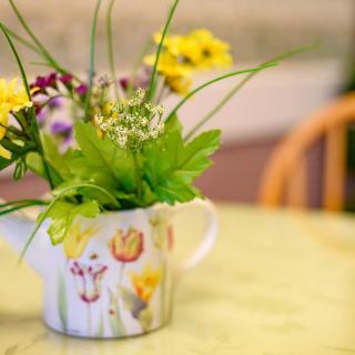 A decorative floral arrangement in a teapot sits on a table.