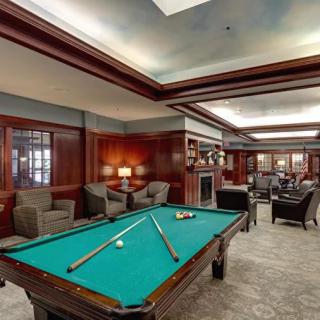 A luxurious billiards room featuring a pool table and comfortable seating with elegant wood paneling.