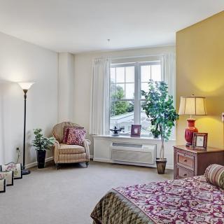 A cozy bedroom with a large window, featuring a bed, chair, and stylish decor.