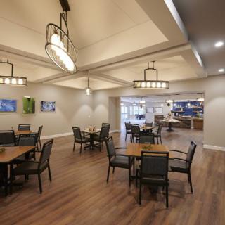 A modern dining area with wooden flooring and elegant chandeliers, featuring several empty tables and chairs.