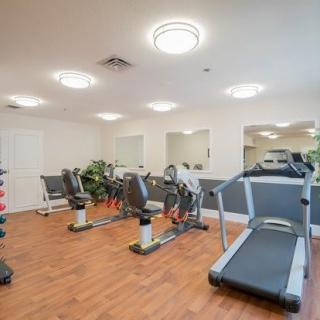 A clean and well-lit gym with treadmills, stationary bikes, and mirrors.