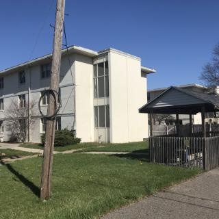 A suburban apartment building with a nearby gazebo and grassy area.