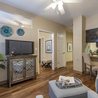 A modern living room with wood flooring, featuring a television on a decorative console, ceiling fan, and tasteful decor in neutral tones.
