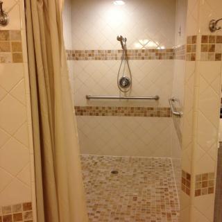 A tiled walk-in shower with a handheld showerhead and grab bar.