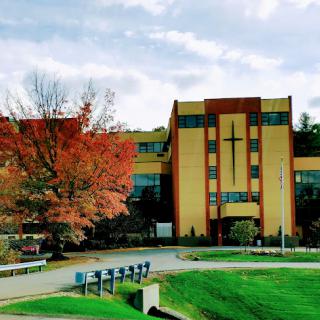 A modern architectural structure with a cross, surrounded by autumn foliage.