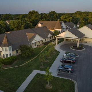 An aerial view of a cluster of buildings surrounded by lush greenery and a small parking lot.