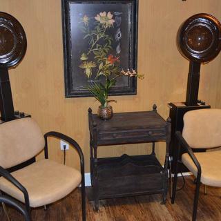 A cozy salon interior featuring two chairs, hair dryers, and a decorative painting.