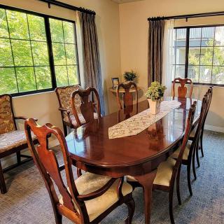 A well-furnished dining room with a large wooden table and chairs surrounded by windows.