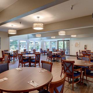 An empty dining area with neatly arranged tables and chairs, featuring modern lighting and a view of the outdoors.