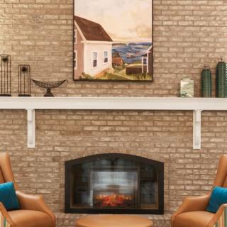 A cozy living room features a brick fireplace adorned with artwork and elegant decorations, surrounded by comfortable seating.