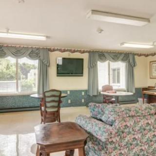 A cozy living room with floral patterned furniture, a television on the wall, and large windows with draped curtains.