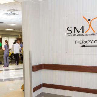 A hospital hallway with a sign pointing to the therapy center and people in the background.