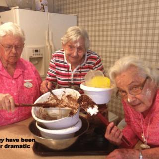 Three elderly women having fun baking together in the kitchen.