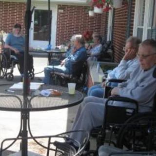 A group of elderly people sitting in wheelchairs on a patio.