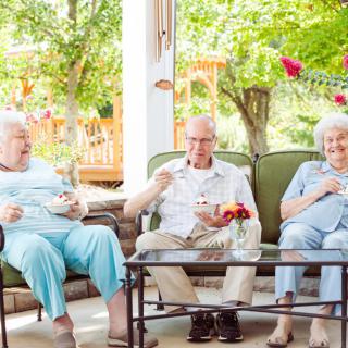 A group of seniors enjoying a relaxed conversation while sitting outdoors in a garden setting.