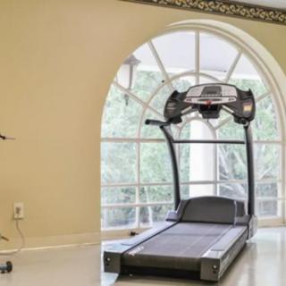 A home gym setup with a treadmill positioned in front of a large arched window.