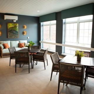 A modern dining and living area with natural light streaming through large windows, featuring stylish furniture and decor.