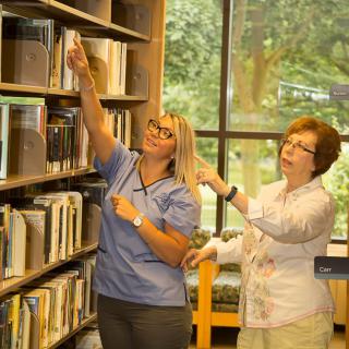 Two women looking at books on a library shelf.