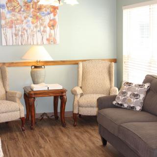 A cozy living room with armchairs, a sofa, and a side table under soft lighting.