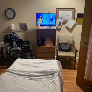 A view of a hospital room featuring a bed, TV, wheelchair, and various documents on the wall.