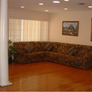A cozy living room featuring a large sectional sofa, hardwood flooring, and natural light filtering through vertical blinds.
