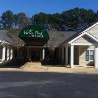 The entrance of a building with an awning labeled 'Valley Park Manor', surrounded by trees.