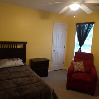 A cozy bedroom with yellow walls, featuring a bed, a red armchair, and a window with curtains.