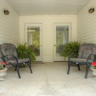 A cozy porch with two cushioned chairs and potted plants, perfect for relaxation.