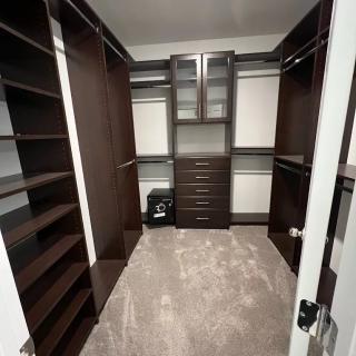 A spacious walk-in closet with dark wood shelving and drawers for organized storage.