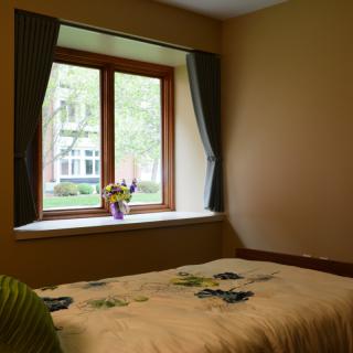 A cozy bedroom featuring a large window with curtains, a bed, and natural lighting.
